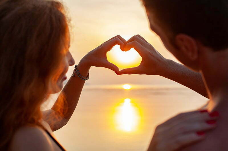 casal romântico fazendo um coração com as mãos no pôr do sol