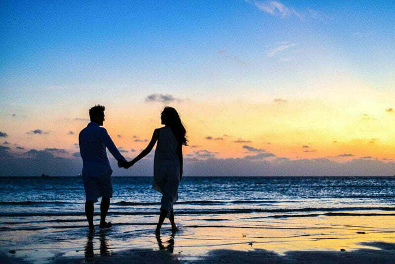 noivos caminhando de mãos dadas na praia ao pôr-do-sol em lua de mel