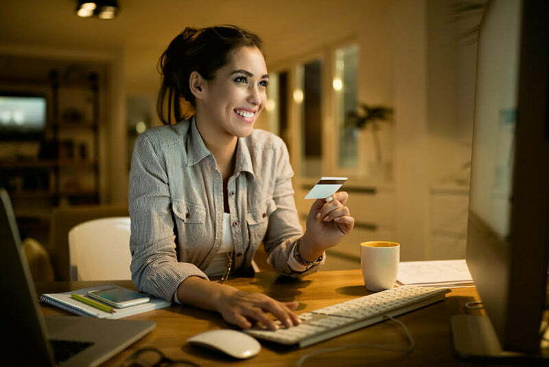 mulher sorrindo e olhando para tela com cartão físico na mão